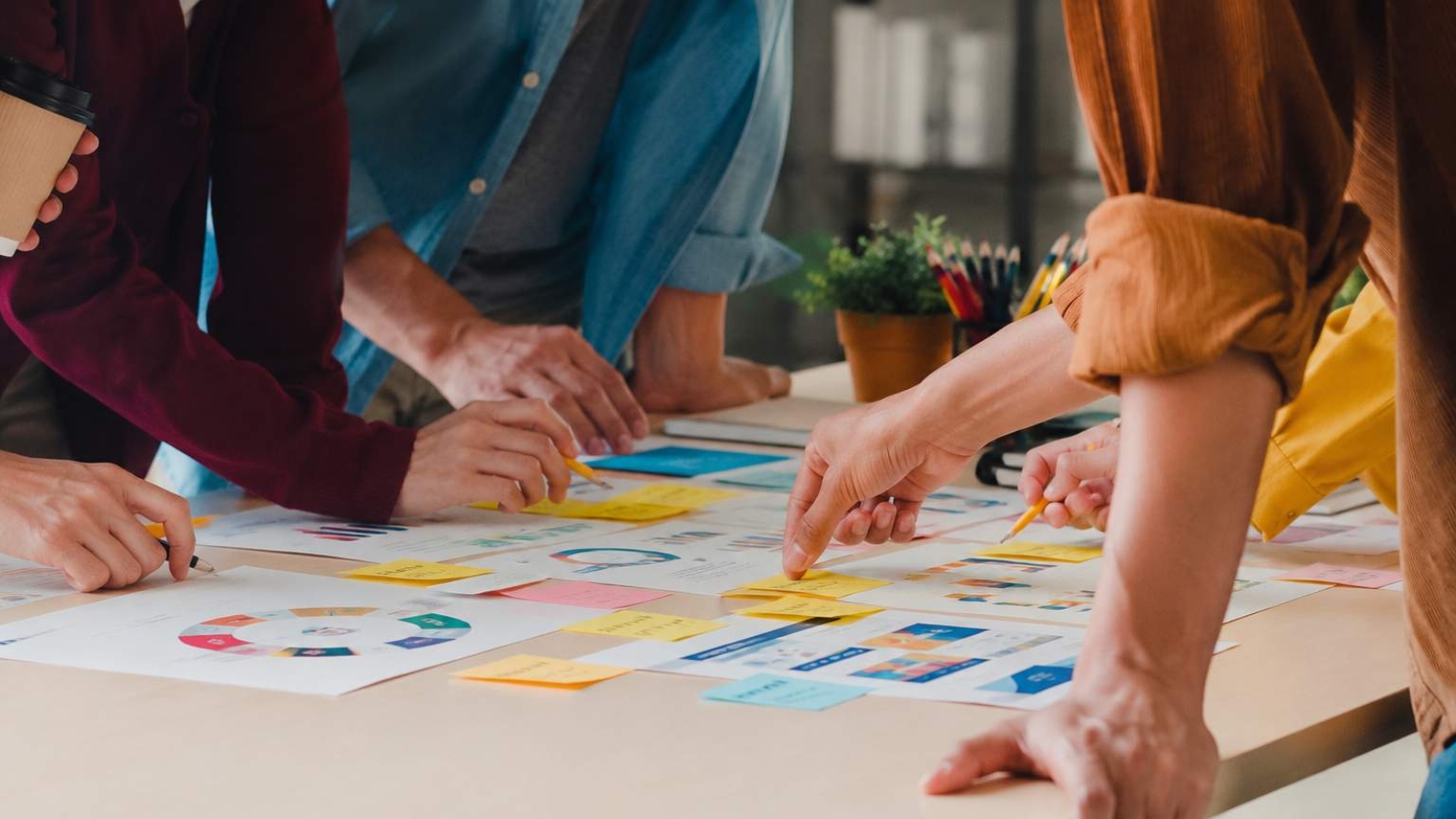 Product Marketing Process team collaborating around a table with charts, sticky notes, and planning documents during a real-world strategy session.