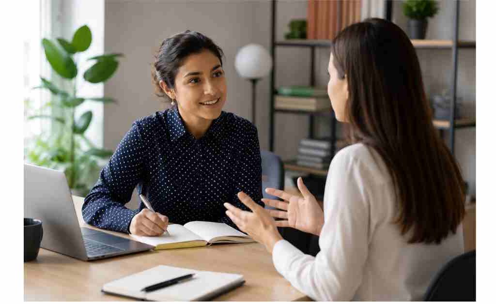 Researcher conducting a one-on-one customer interview in a professional office, actively listening, asking open-ended questions, and taking notes to gather valuable customer insights.